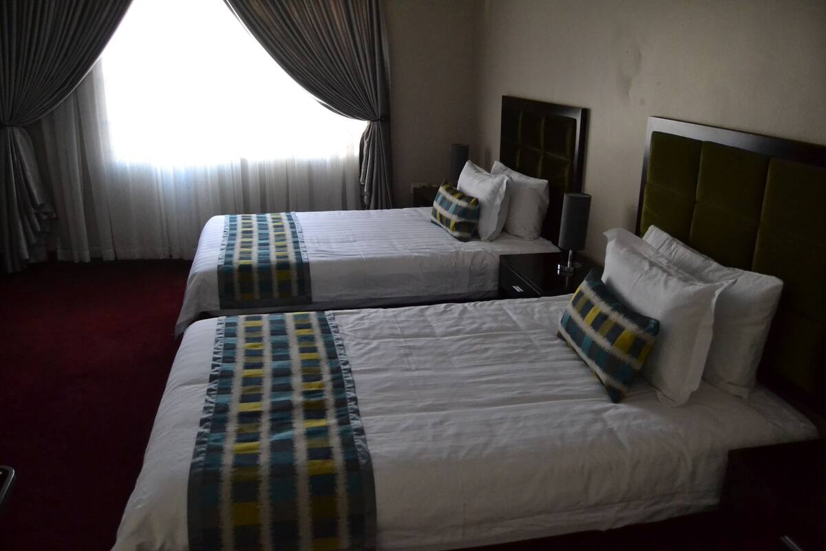 Two single beds with headboards, a window with curtains, and a red carpet.