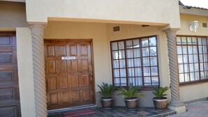 A reception door with a sign, potted plants, and a window with curtains. - Triple Palms Bed and Breakfast (Gaborone)