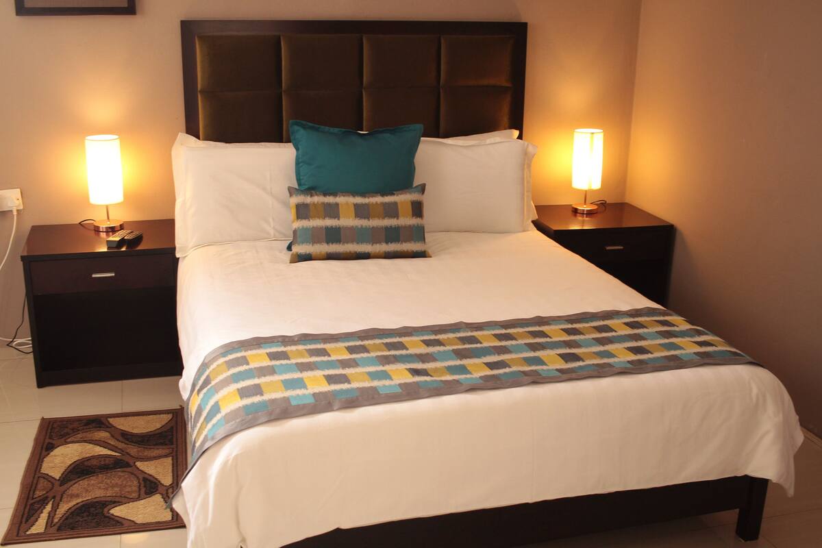 A neatly made bed with a checkered throw blanket, two bedside lamps, and a headboard.