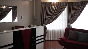 A room with a kitchenette, a red sofa, and a window with curtains. - Triple Palms Bed and Breakfast (Gaborone)