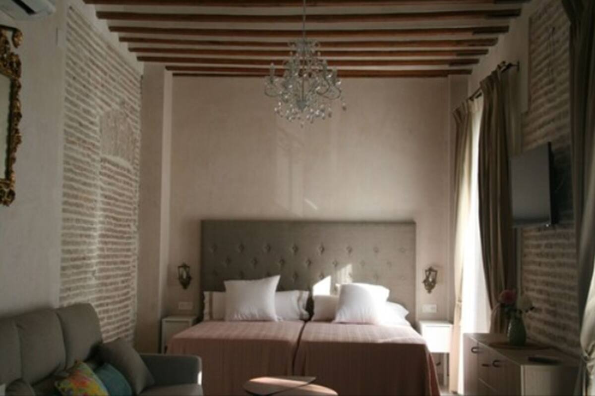 Un dormitorio con cama, lámpara de araña, televisor y ventana.