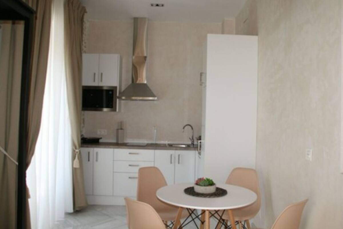 Una cocina moderna con armarios blancos, una campana extractora de acero inoxidable y un comedor con una mesa redonda y sillas.