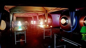 Un espace sous tente aménagé avec des tables et des chaises, une petite scène et du matériel de sonorisation.