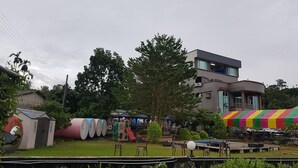 Un bâtiment moderne doté d’un toit plat et de grandes fenêtres, entouré de verdure et d’aires de jeux pour enfants.