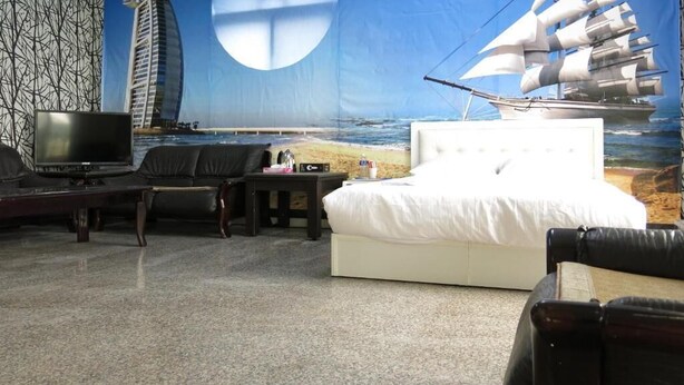 Une chambre d’hôtel avec une grande fresque représentant un voilier et un bâtiment, un lit, une télévision et un coin salon.