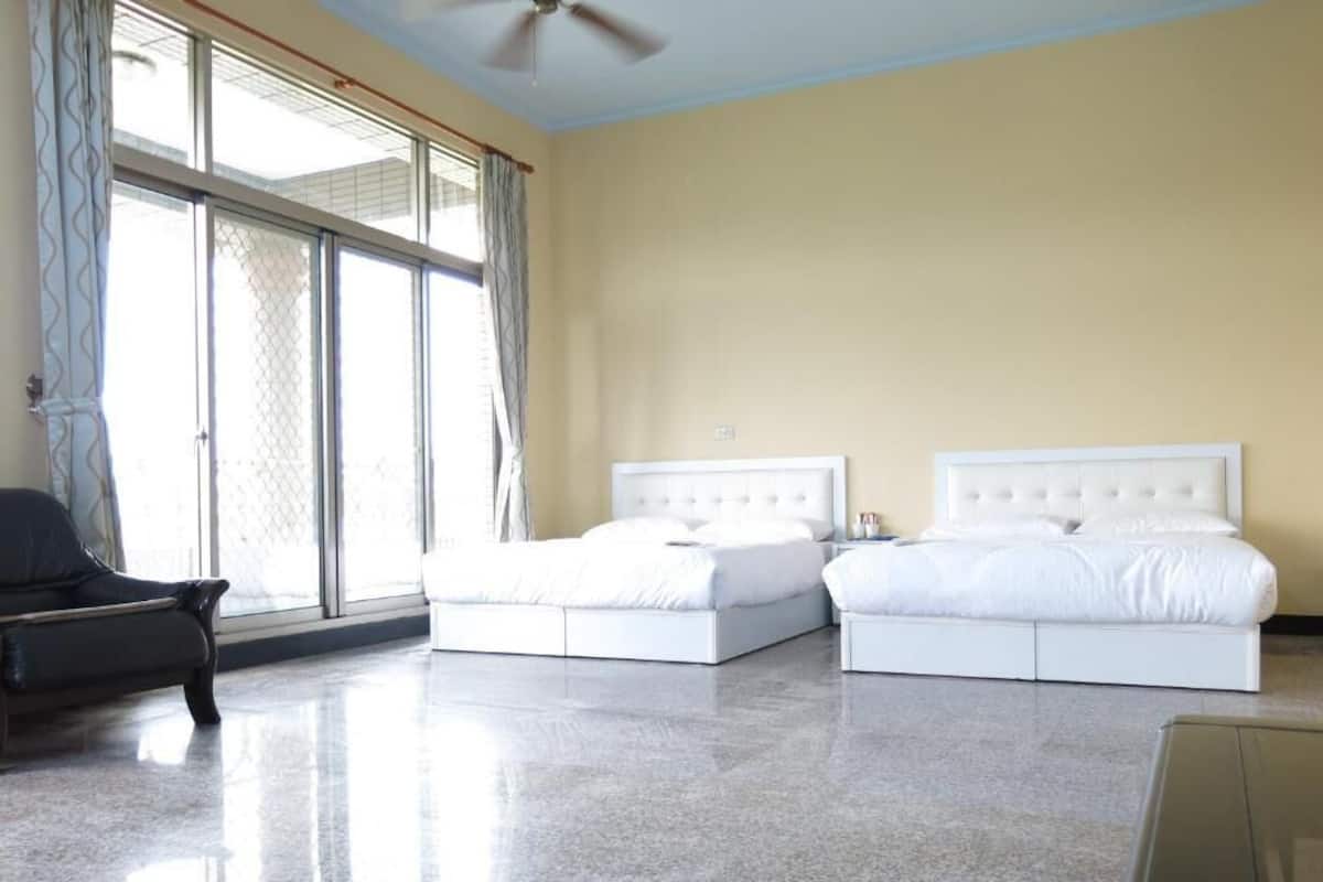 A hotel room with two beds, a ceiling fan, and large windows with curtains.