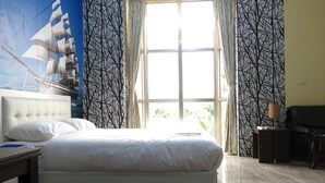 Une chambre à coucher avec un grand lit, une fenêtre avec des rideaux, une fresque murale et un bureau avec une lampe.
