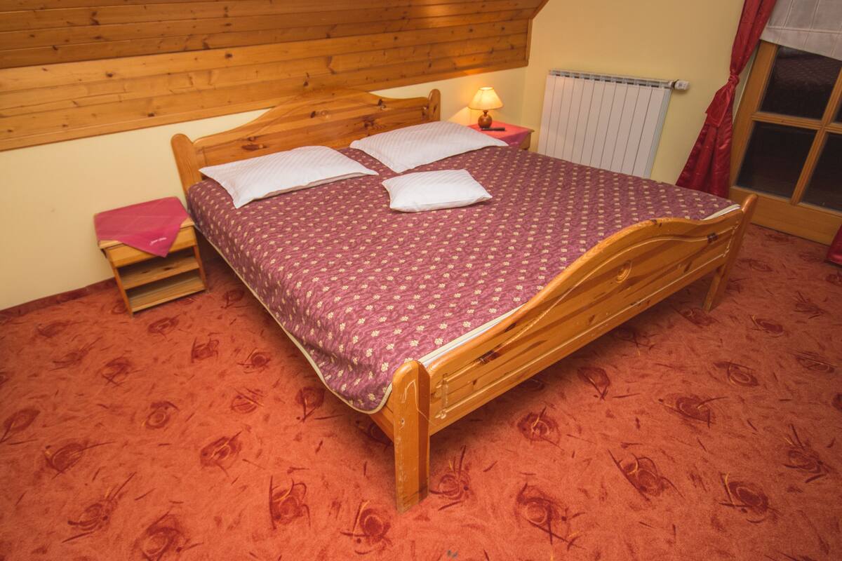 A wooden bed with a patterned bedspread in a room with a red carpet and wooden walls.