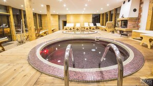Un jacuzzi circular con borde de azulejos, rodeado de una terraza de madera y sillones de descanso.