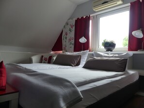 A bedroom with a bed, red curtains, a window with a view, and an air conditioning unit. - Zuhause bei Hoffmann (Hamminkeln)