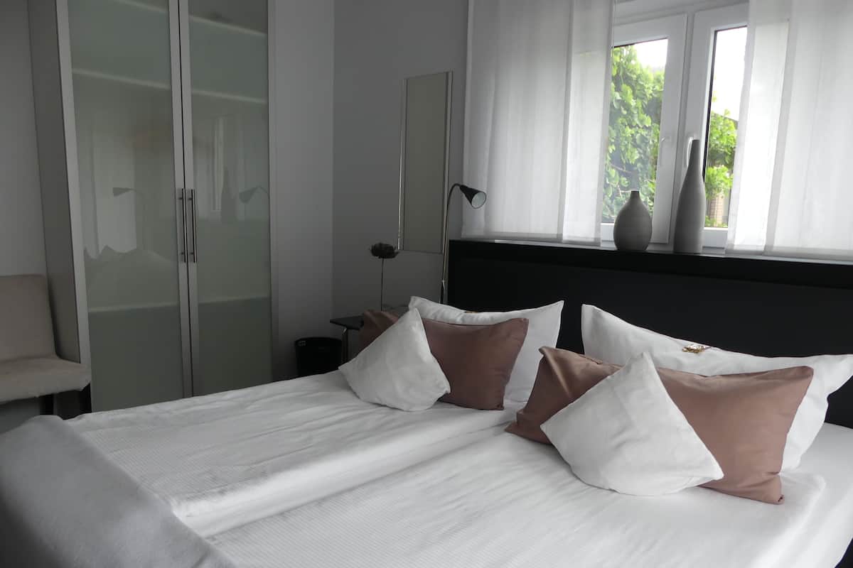 A neatly made bed with white and brown pillows, a bedside lamp, and a window with a view of greenery.