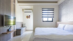 A modern bedroom with a large bed, a flat-screen TV mounted on the wall, a small seating area, and a window with blinds. - Jialai Homestay (Magong)