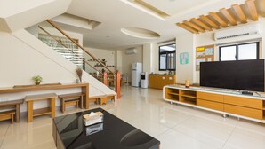 A modern living room with a staircase, a flat-screen TV, wooden furniture, and a kitchen area. - Jialai Homestay (Magong)