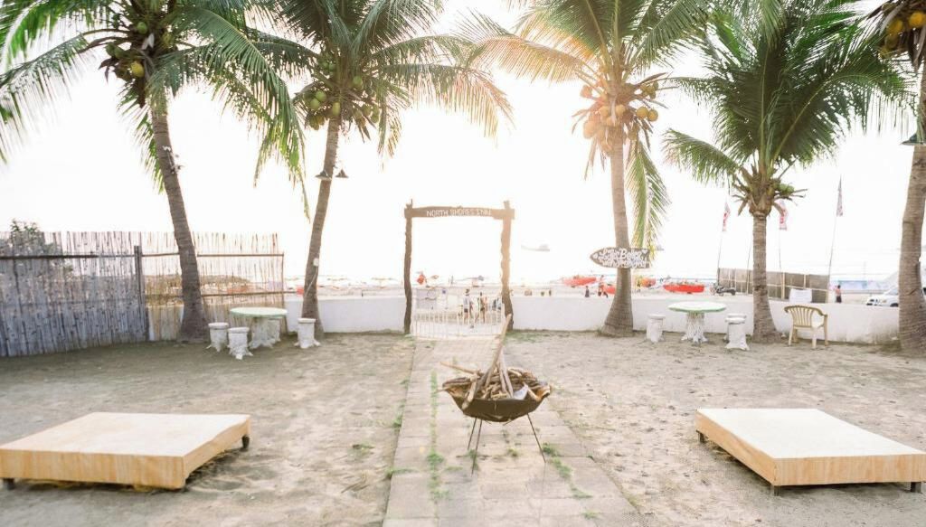 An outdoor seating area with a wooden table and chairs, a fire pit, and palm trees.