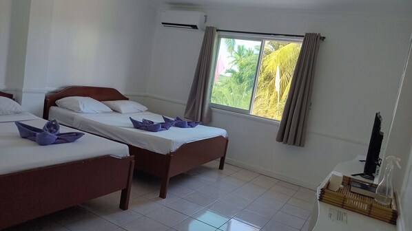 A hotel room with two beds, a window with curtains, a TV, and a small table with toiletries. - North Shores Inn (Currimao)