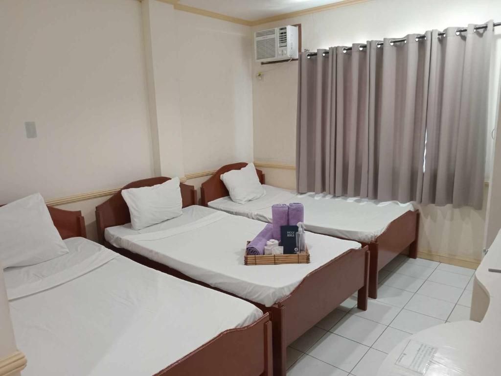 Una habitación de hotel con dos camas individuales, una mesita con artículos de aseo y un ventanal con cortinas.
