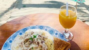 A table with a plate of food and a drink, a beach in the background, and a gate leading to the beach.