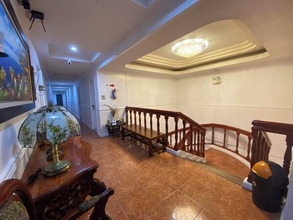 A hallway with a wooden staircase, a chandelier, a fire extinguisher, and a painting on the wall. - North Shores Inn (Currimao)
