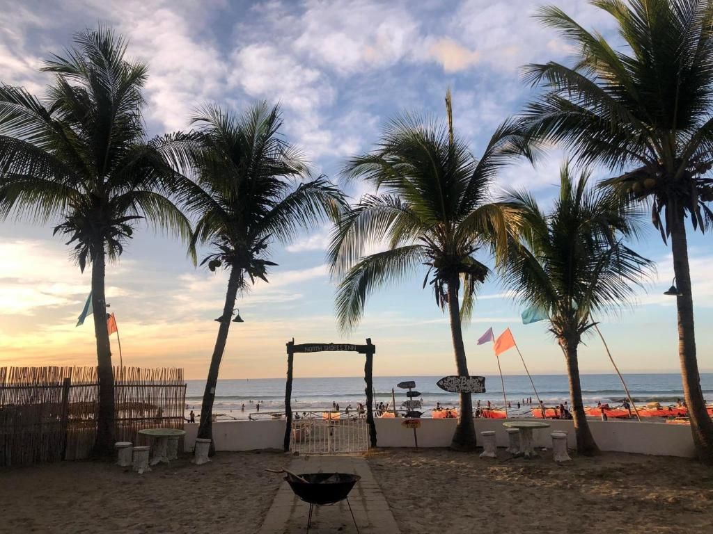 Una playa con palmeras, una parrilla y una valla.