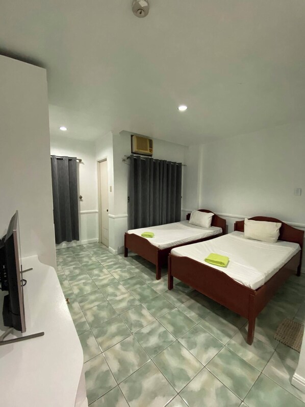 Une chambre d’hôtel avec deux lits, une télévision et une salle de bain avec un rideau de douche.