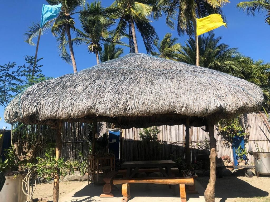 A thatched-roof outdoor seating area with a wooden bench, surrounded by palm trees and a bamboo fence.
