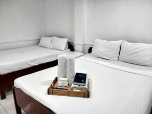 Habitación de hotel con dos camas individuales, una mesita de noche con artículos de aseo y una bandeja con toallas y un libro.