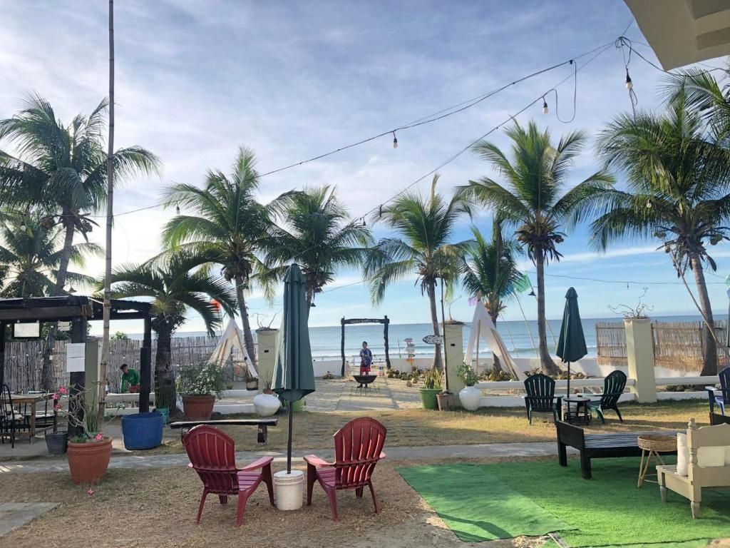 An outdoor seating area with chairs and tables, palm trees, and a view of the ocean.