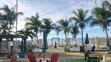 An outdoor seating area with chairs and tables, palm trees, and a view of the ocean.