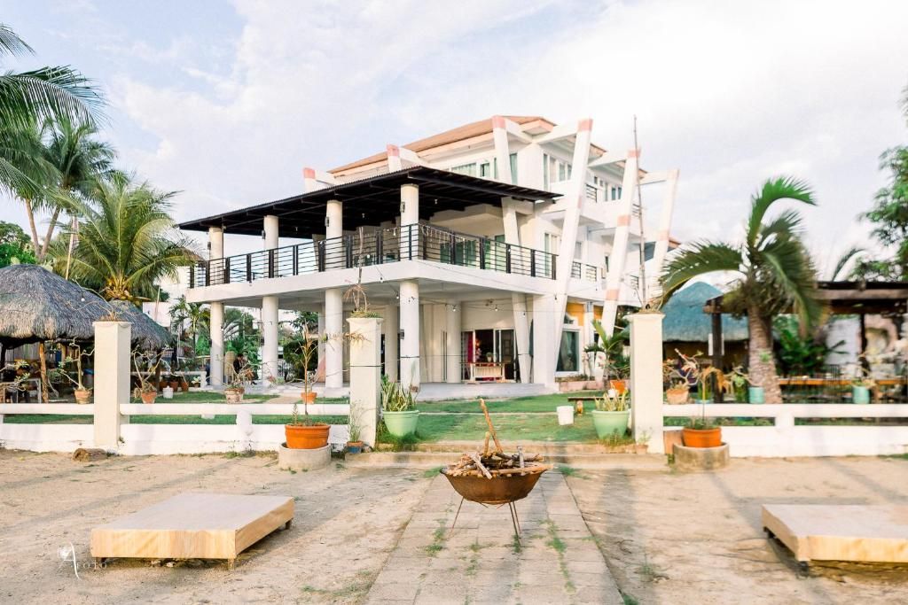 Un hotel de varios pisos con balcón, mobiliario exterior y una estructura de techo de paja.