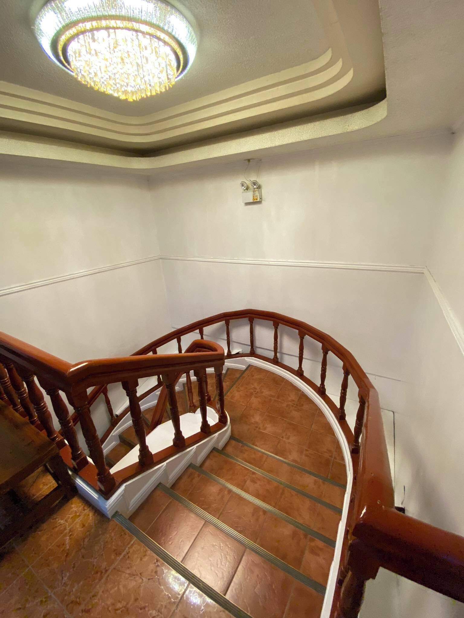 Una escalera con barandillas de madera y balaustrada de vidrio, que conduce a un rellano con una araña.