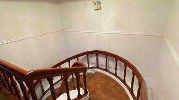 Una escalera con barandillas de madera y balaustrada de vidrio, que conduce a un rellano con una araña.