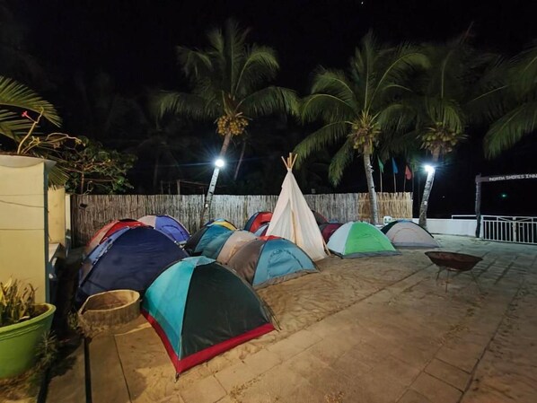 A series of tents arranged on a paved area with palm trees in the background.
