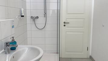 A bathroom with a white sink, a glass shower enclosure, and a white door.