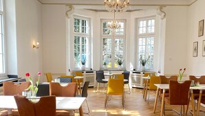 A spacious dining area with high ceilings, large windows, and a chandelier.
