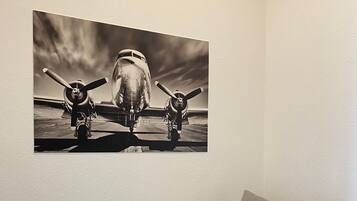 A room with a gray sofa and a large black-and-white airplane painting on the wall.