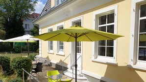 An outdoor patio with yellow and white walls, green and white outdoor furniture, and a yellow umbrella.
