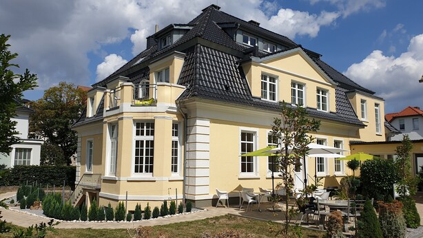 A large, two-story house with a balcony, a patio with outdoor seating, and a well-maintained garden.