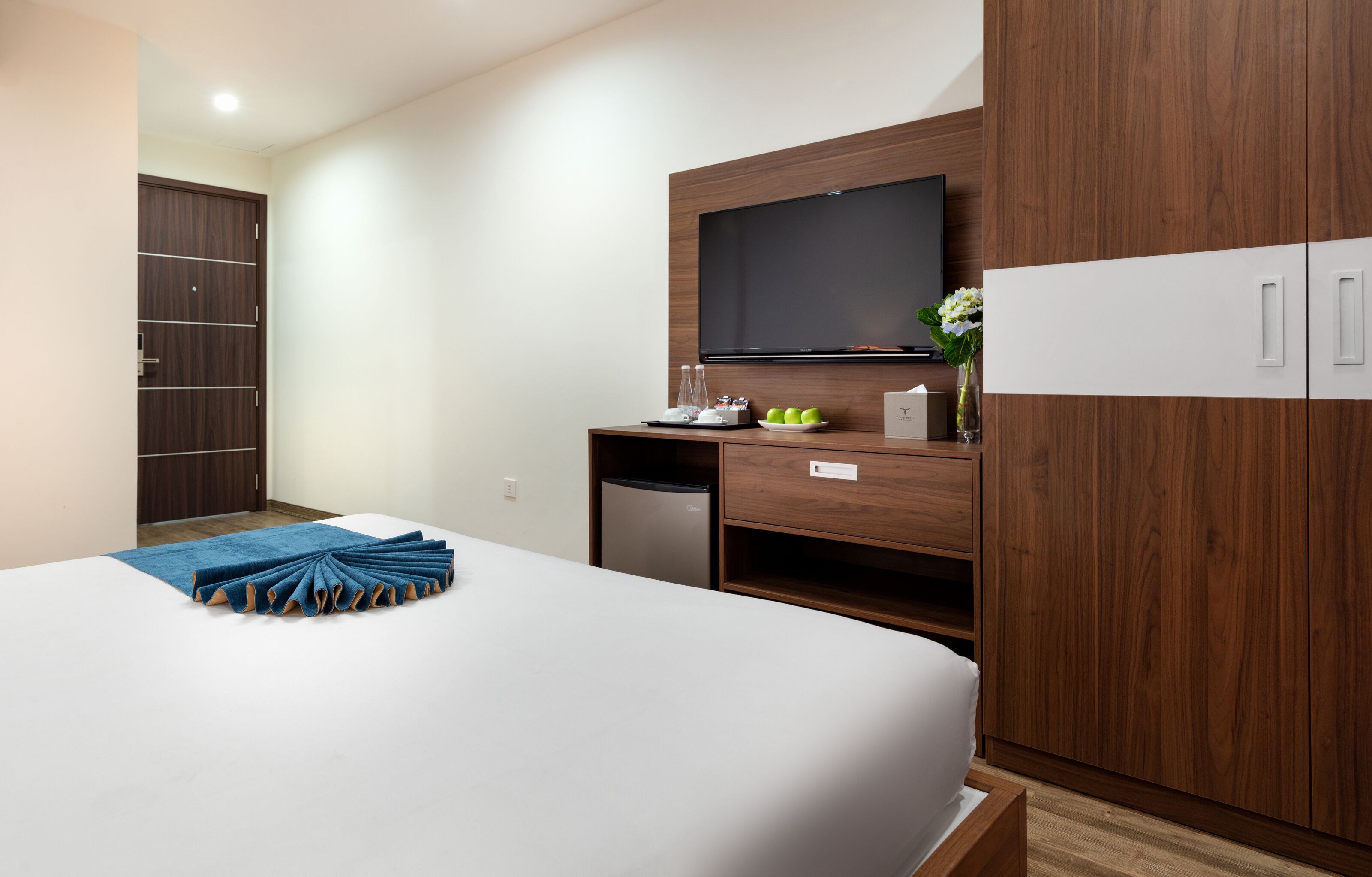 A hotel room with a bed, a TV, a minibar, and a wardrobe.