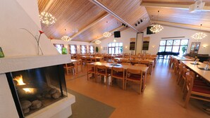 A spacious dining area with multiple tables and chairs, a fireplace, and large windows allowing natural light.