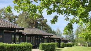 A row of dark-colored cabins with tiled roofs, surrounded by well-maintained hedges and trees.
