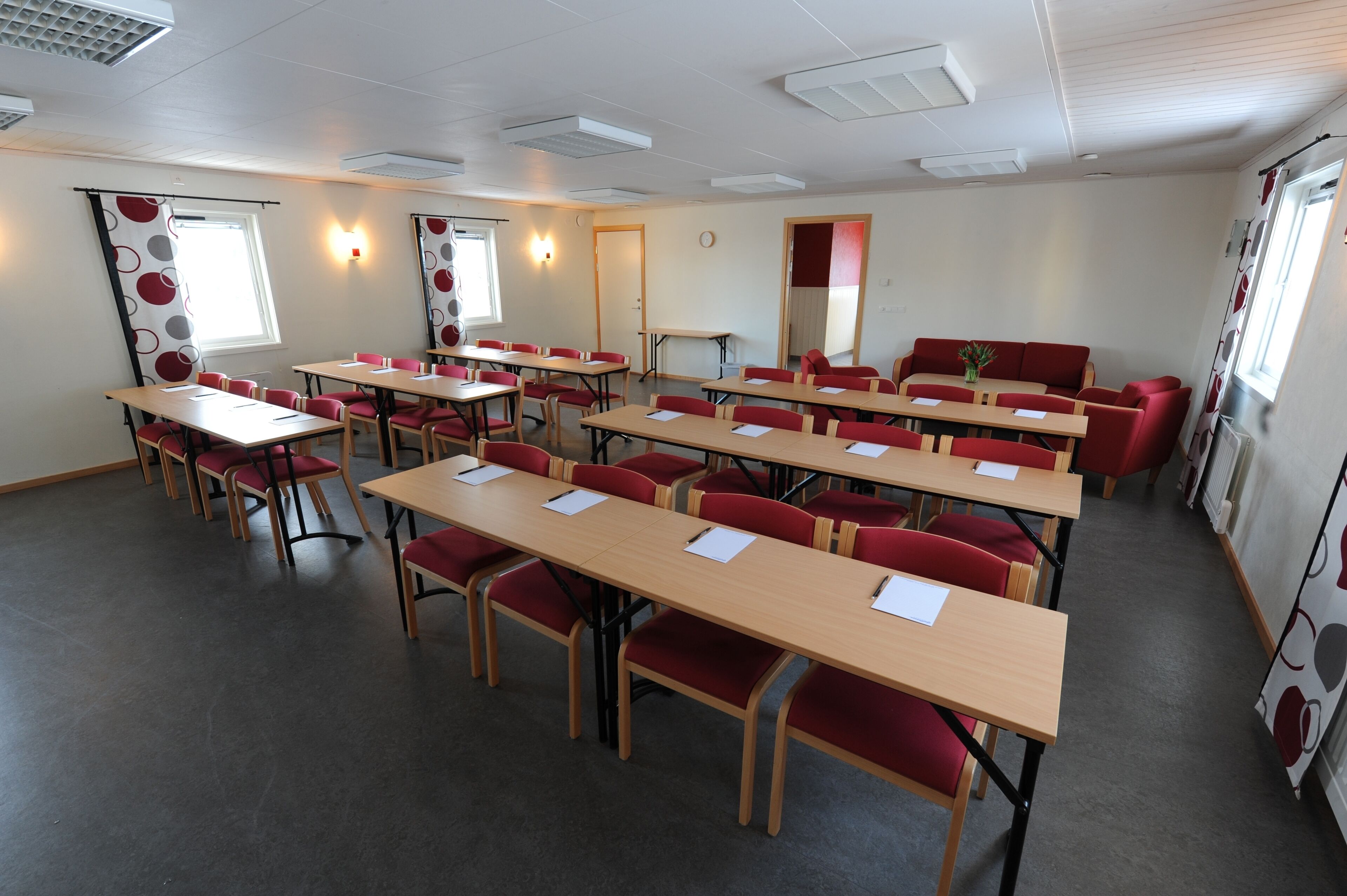 A conference room with multiple tables and chairs, a clock on the wall, and a window with curtains.