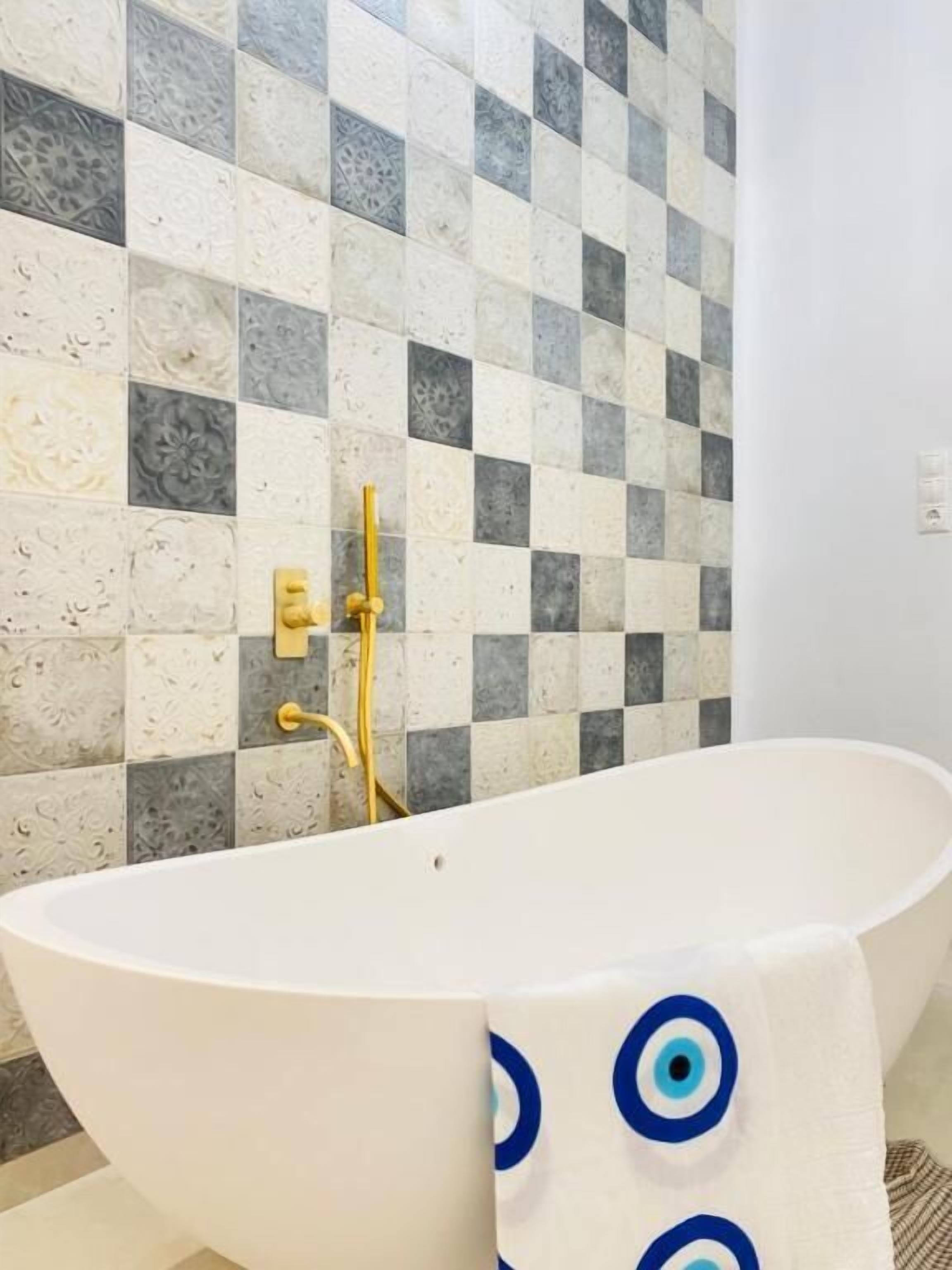 Un baño con una bañera independiente, salpicadero de baldosas de cuadros y un grifo dorado.