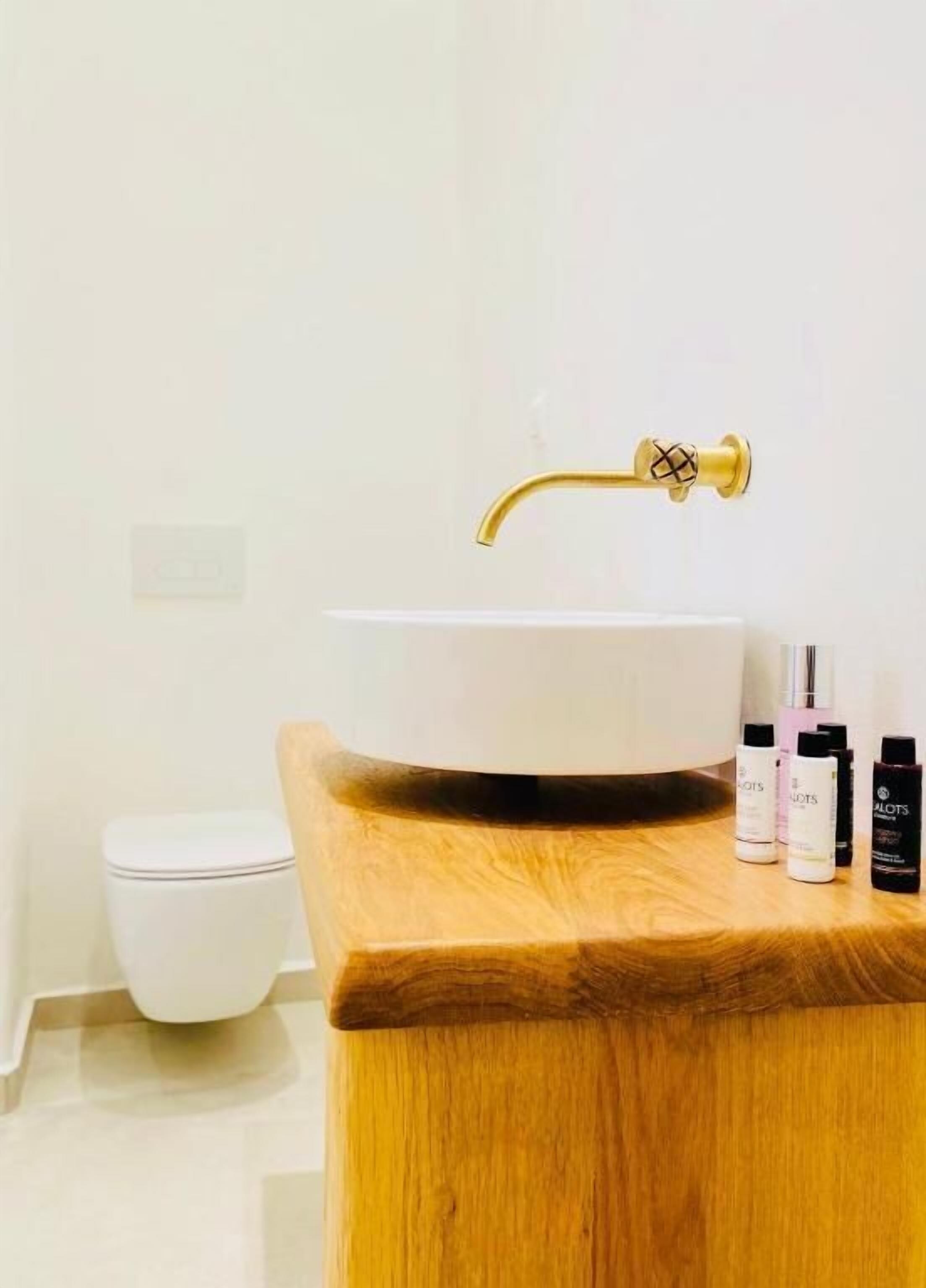 A bathroom with a wooden vanity, a white sink with a gold faucet, and toiletries on the counter.