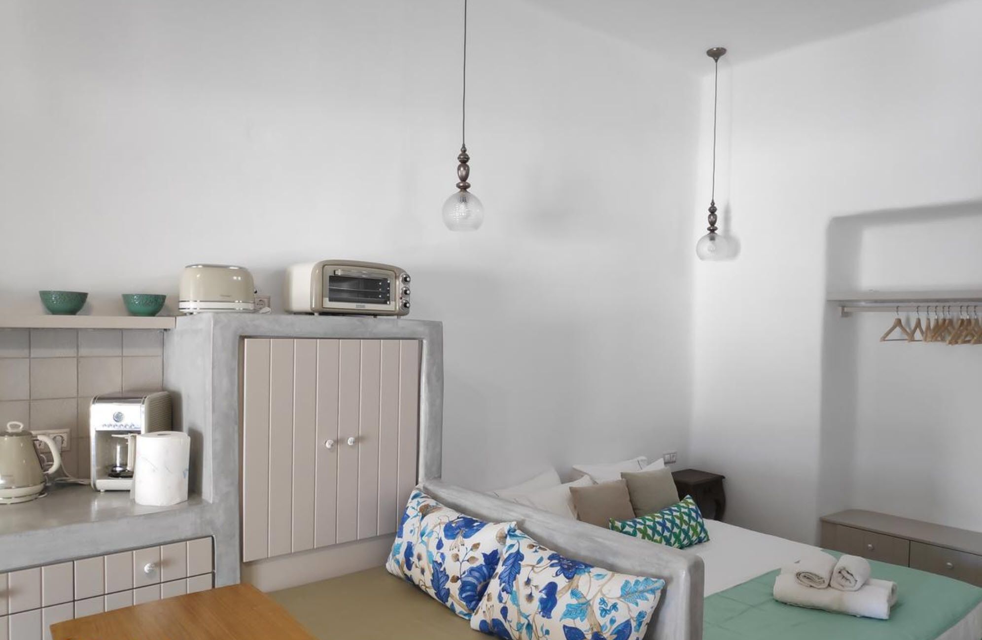 A compact kitchenette with a built-in oven, a coffee maker, and a toaster. There is a bed with a floral pillow and a green blanket.
