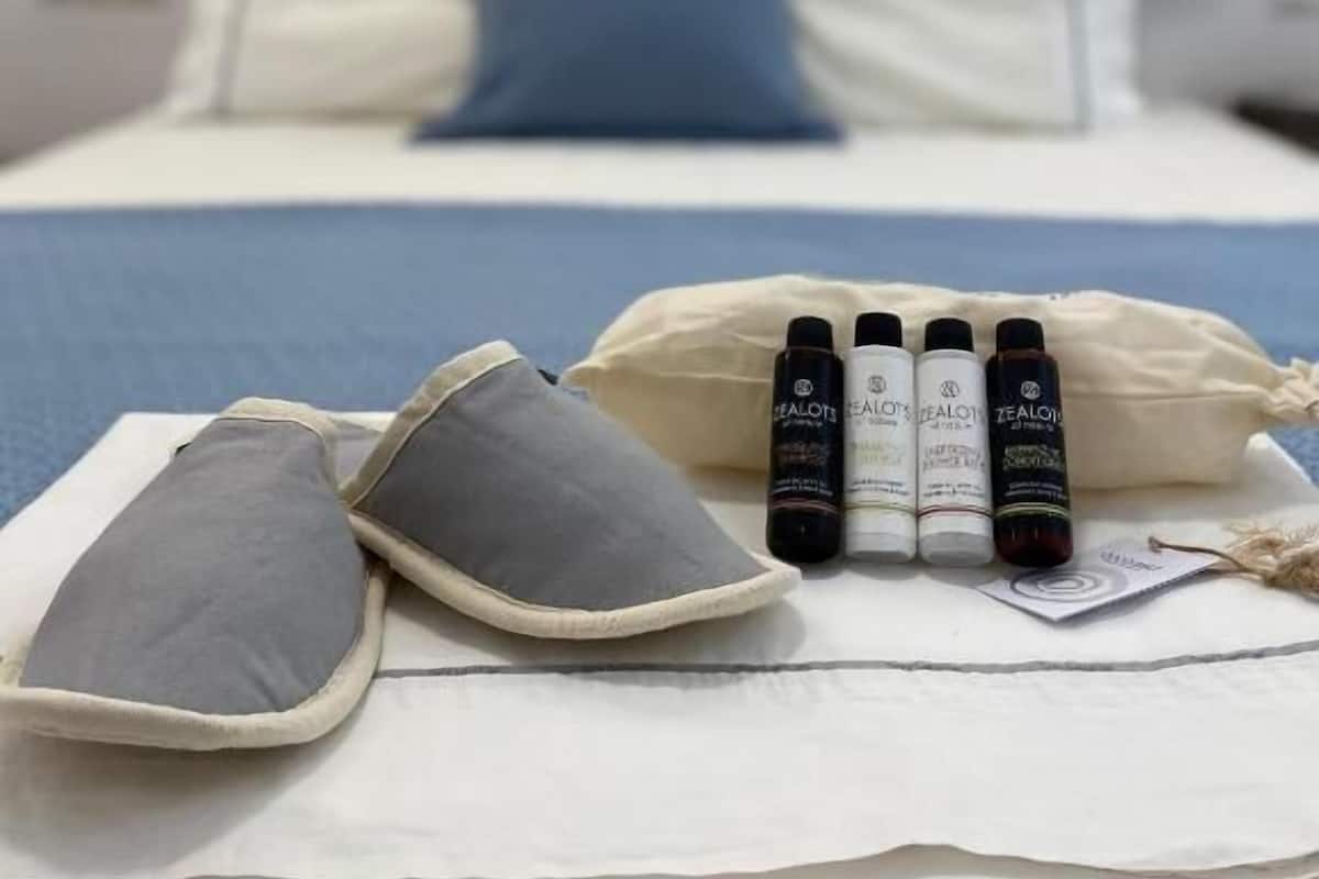 A neatly made bed with pillows, a blue pillow, and a set of skincare products on a white bedsheet.