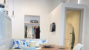 A modern dining area with a round wooden table, two light blue chairs, a sofa with a floral cushion, and a wardrobe with a mirror.