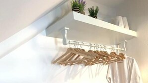 A minimalist room with a white wall, a wooden floor, a white shelf with a hanging rack, and a small shelf with decorative items.