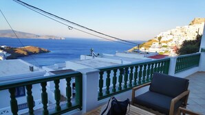 A balcony with a view of the sea and a white building in the distance.