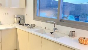 A modern kitchen with a large window, white cabinets, a stainless steel coffee maker, and a decorative pumpkin.