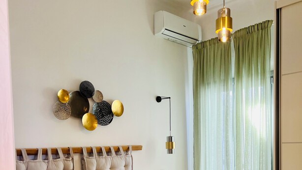 A neatly made bed with a tufted headboard, a bedside table with a lamp, and a wall-mounted air conditioner.